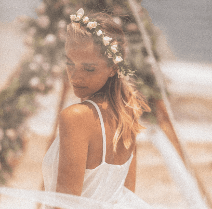 back view of blonde woman in a wedding dress with a white rose crown with faded background of wedding decorations